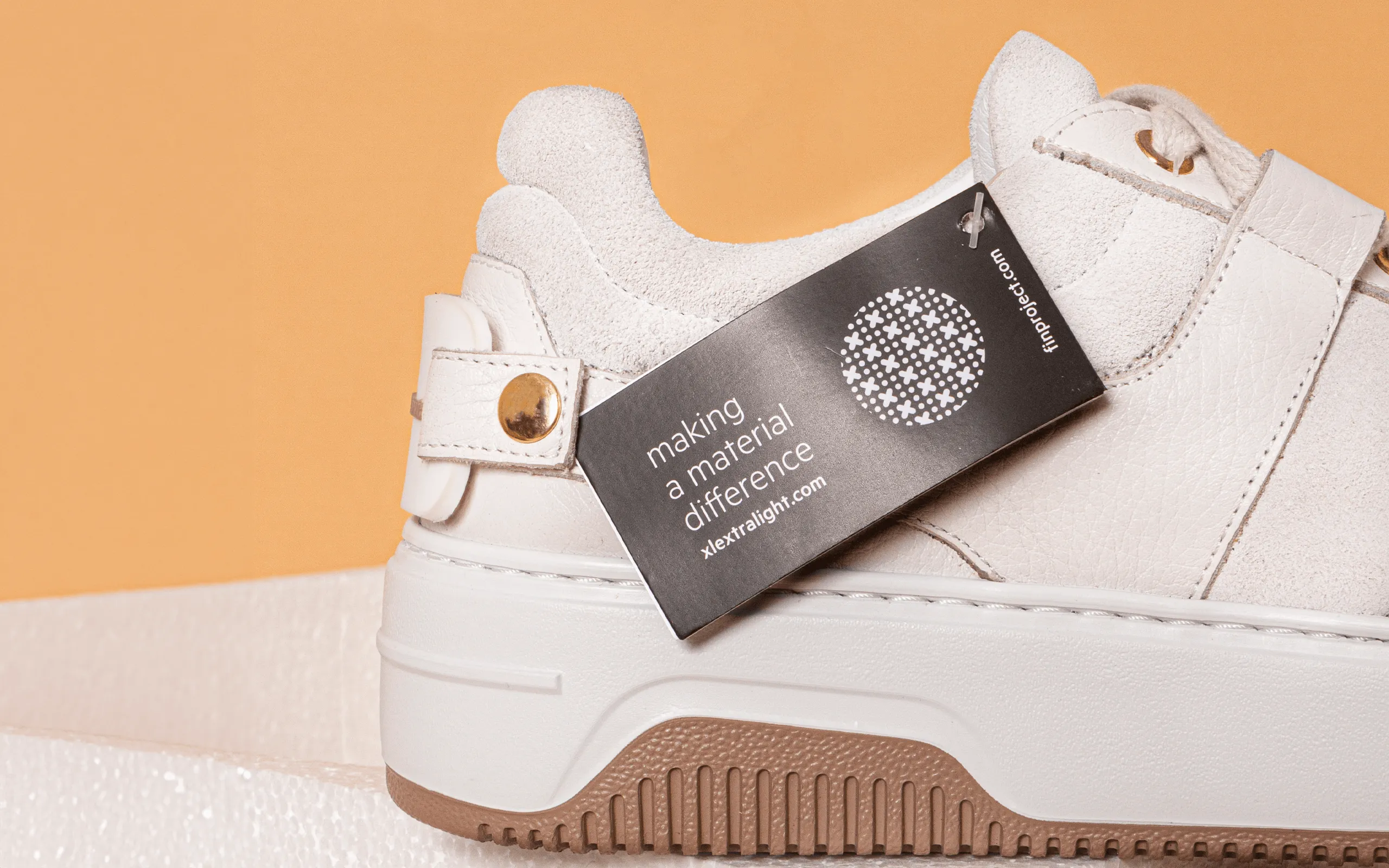 Weißer Lederschuh mit Purde's Anhänger vor orangem Hintergrund